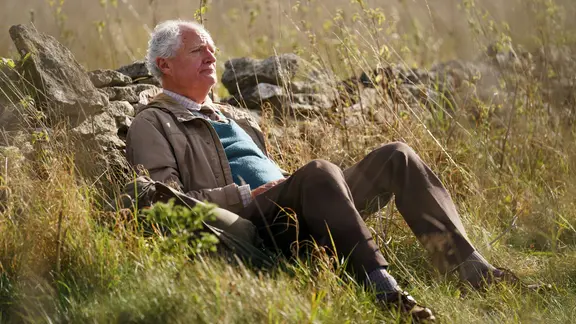 Harold (Jim Broadbent) genießt seinen Aufbruch. | Embankment Films/David Gennard Ein alter Man sitzt auf einer Wiese und lehnt sich an eine Steinmauer
