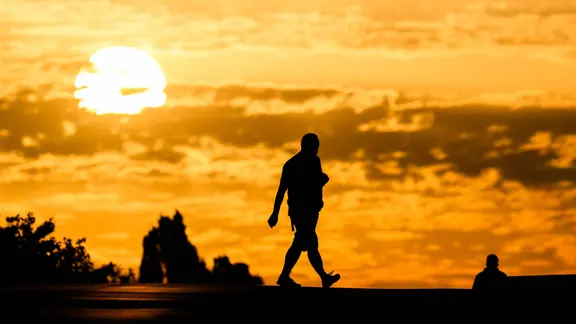 Ein Mann geht bei Sonnenaufgang über eine Straße in der Region Hannover. | dpa-Bildfunk/Julian Stratenschulte Ein Mann geht bei Sonnenaufgang über eine Straße in der Region Hannover.