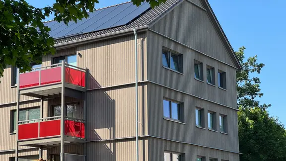 Die Mieter haben nun größere Balkone. | NDR, Sabine Hausherr Ein mit Holz verkleidetes Haus mit roten Balkonen.