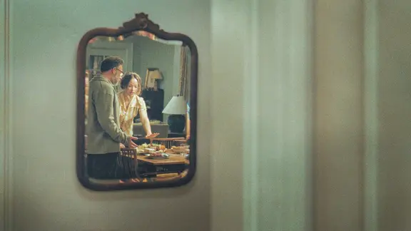 Olivia Wilde spielt die vernachlässigte Ehefrau Angela und Seth Rogan ihren Mann Joe. | Tobis Film In einem Spiegel sind eine Frau und ein Mann an einem Tisch stehend zu sehen.