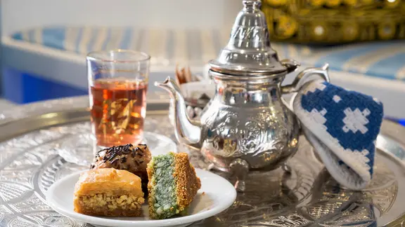 Eine orientalische, silber Kanne auf einem silbernen Tablett, davor ein Teller mit Gebäck, dahinter ein Teeglas | picture alliance / FoodCollection | Afanasyeva, Oxana Eine orientalische, silber Kanne auf einem silbernen Tablett, davor ein Teller mit Gebäck, dahinter ein Teeglas