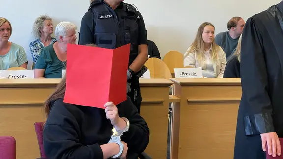 Die Mutter lehnte es ab ihre Tochter zu stillen und war mit der Erziehung überfordert so heißt es in der Urteilsbegründung. | NDR, Sven Jachmann Eine Frau bei Gericht hält sich eine rote Akte vor das Gesicht.
