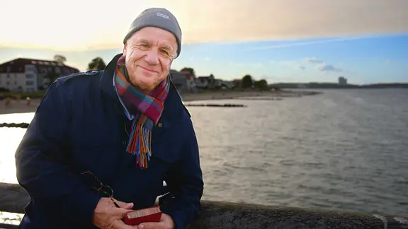 Hubertus Meyer-Burckhardt mit einem historischen Reiseführer auf der Seebrücke in Niendorf. | NDR/Stefan Wieduwilt Hubertus Meyer-Burckhardt mit einem historischen Reiseführer auf der Seebrücke in Niendorf.