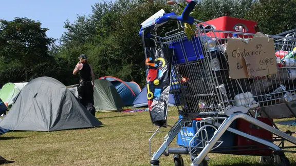 Ein Teilnehmer des Punk-Protestcamps geht hinter einem Einkaufswagen und zwischen Zelten über die Camp-Wiese | picture alliance/dpa | Lea Albert Ein Teilnehmer des Punk-Protestcamps geht hinter einem Einkaufswagen und zwischen Zelten über die Camp-Wiese