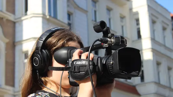 In Leipzig können junge Menschen erfahren, wie man Video-Reportagen dreht. | Villa Leipzig Eine junge Frau schaut durch eine professionelle Videokamera.