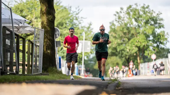Metal trifft Morgenrunde - eingefangen auf der Hauptstraße in Wacken. | NDR / Dominik Dührsen Zwei Männer joggen durch Wacken.