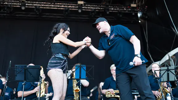 Die "neue Dirigentin" und der Chef der Wacken Firefighters auf der Wackinger Stage. | NDR, Alexander Mühlhausen Zwei Persoenn klatschen sich auf einer Bühne ab