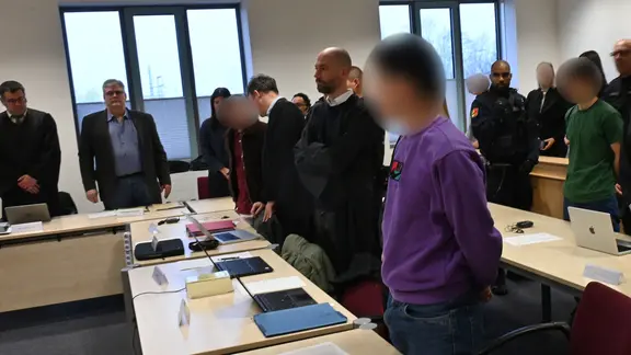 Mehrere Angeklagte stehen und sitzen neben ihren Verteidigern im Gerichtssaal des Landgerichts Itzehoe. | dpa-Bildfunk, Felix Müschen Mehrere Angeklagte stehen und sitzen neben ihren Verteidigern im Gerichtssaal des Landgerichts Itzehoe.