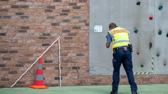 Ein Kriseninterventionsteam betreute Schülerinnen und Schüler einer Leipziger Grundschule, nachdem ein Auto das Schultor durchbrochen hatte. | EHL Media Ein Polizist misst neben einem roten Warnkegel mit einem großen Zollstock die Unfallstelle auf einem Schulhof aus