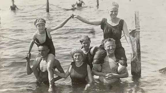 Eine Gruppen von Menschen steht in der Ostsee, zwei Männer tragen Kinder auf den Schultern, vermutlich 1920er-Jahre | Jürgen Kraft Eine Gruppen von Menschen steht in der Ostsee, zwei Männer tragen Kinder auf den Schultern, vermutlich 1920er-Jahre