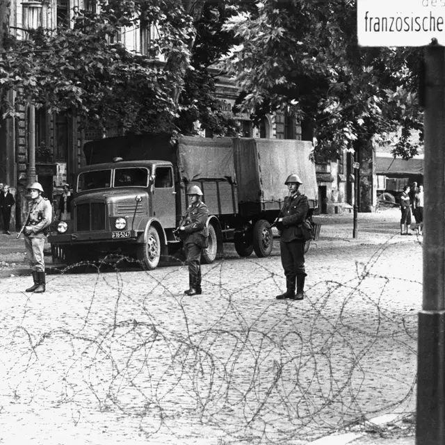 Volkspolizisten am 13. August 1961 hinter einer Stacheldraht-Absperrung in der Bernauer Straße. | picture alliance / dpa | Konrad Giehr Volkspolizisten stehen am 13. August 1961 hinter einer Stacheldraht-Absperrung in der Bernauer Straße in Berlin.