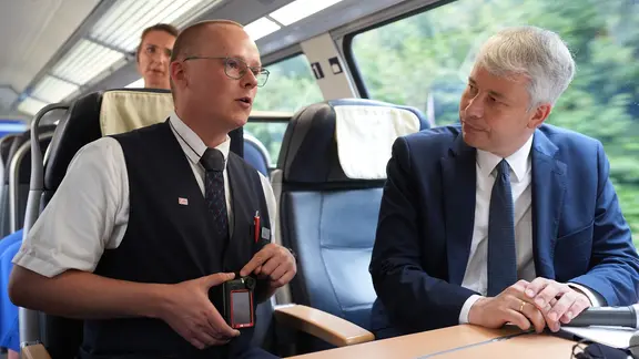 Sicherheit im Zug sei kein Randthema, so Bilger. Er kündigte Gespräche der Regierung an. | Marcus Brandt/dpa Bundesverkehrsminister Bilger spricht mit einem Bahnmitarbeiter in einem Zug.
