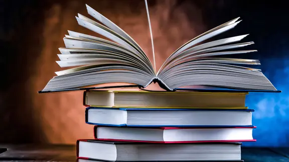 Ein Stapel Bücher, auf dem ein einzelnes aufgeschlagenes Buch liegt. | iStock Ein Stapel Bücher, auf dem ein einzelnes aufgeschlagenes Buch liegt.