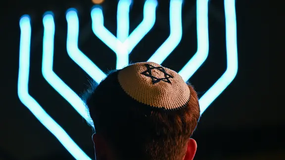 Ein Mann, der eine Kippa mit Davidstern trägt vor einem Chanukka-Leuchter | picture alliance/dpa Ein Mann, der eine Kippa mit Davidstern trägt vor einem Chanukka-Leuchter