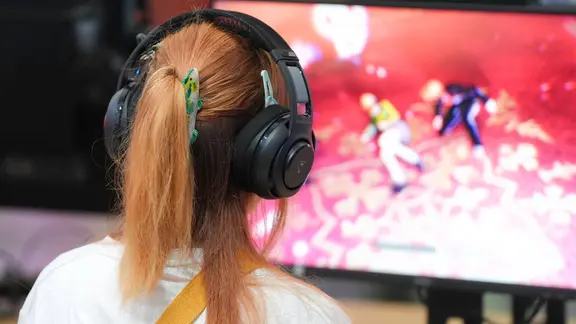 Eine Frau mit Kopfhörern sitzt vor einem Gaming-PC und spielt ein Videospiel | IMAGO / Political-Moments Eine Frau mit Kopfhörern sitzt vor einem Gaming-PC und spielt ein Videospiel