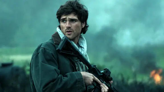 Szene aus dem Film "Das Ende der Sterne": Ein junger Mann steht mit einer Waffe in der Hand auf einem Feld und blickt besorgt zur Seite | The Walt Disney Company Szene aus dem Film "Das Ende der Sterne": Ein junger Mann steht mit einer Waffe in der Hand auf einem Feld und blickt besorgt zur Seite