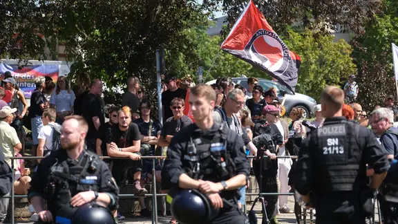 An Gegendemonstrationen beteiligten sich laut Polizei 400 Menschen. | picture alliance/dpa | Sebastian Willnow Hinter einer Reihe von Polizisten schwenken Demonstranten eine Fahne der Antifa.
