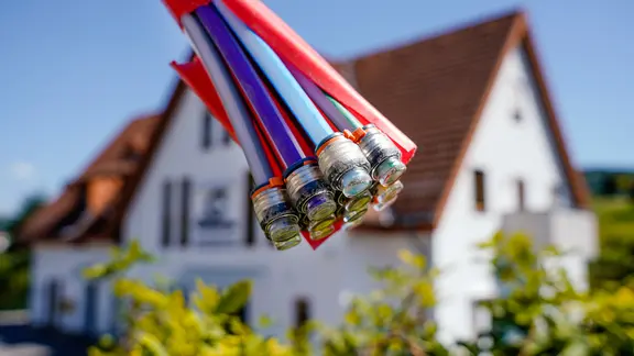 Ein Bündel Glasfaserkabel vor einem Wohnhaus. | picture alliance, Uwe Anspach Ein Bündel Glasfaserkabel vor einem Wohnhaus.