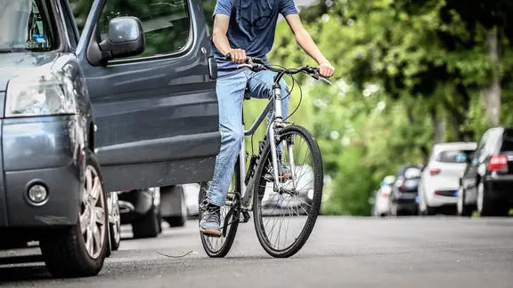 Plötzlich aufgerissene Autotüren sind für Radfahrer eine große Gefahr (Symbolbild). | IMAGO / Funke Foto Services Ein Radfahrer versucht einer geöffneten Autotür auszuweichen.