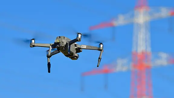 Eine Drohne fliegt in der Nähe einer Stromleitung. | picture alliance / Daniel Kubirski Eine Drohne fliegt in der Nähe einer Stromleitung.