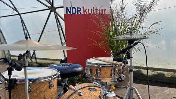 Ein Schlagzeug steht vor einem Banner von NDR Kultur und einer Topfplanze. | NDR , Tom Holste Ein Schlagzeug steht vor einem Banner von NDR Kultur und einer Topfplanze.