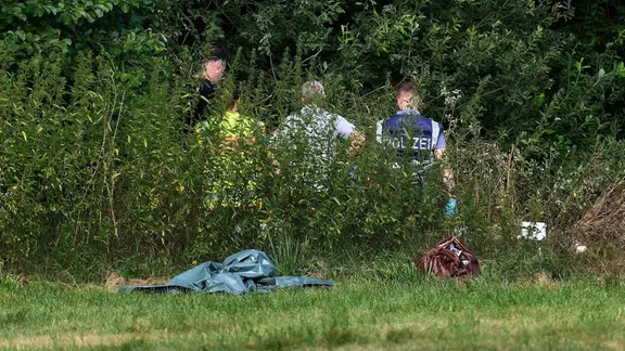 Mitarbeiter der Bundesstelle für Flugunfalluntersuchung haben Untersuchungen zum Unfallgeschehen aufgenommen. | Marcus Golejewski Mehrere Personen mit Rücken zur Kamera hinter hohen Brennesseln