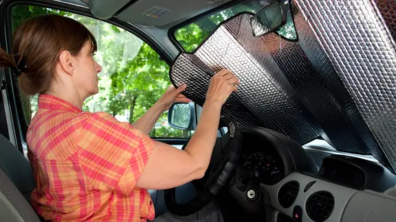 Eine Frau breitet eine Hitzeschutzfolie vor der Windschutzscheibe ihres Autos aus. | picture alliance / dpa Themendienst | Kai Remmers Eine Frau breitet eine Hitzeschutzfolie vor der Windschutzscheibe ihres Autos aus.