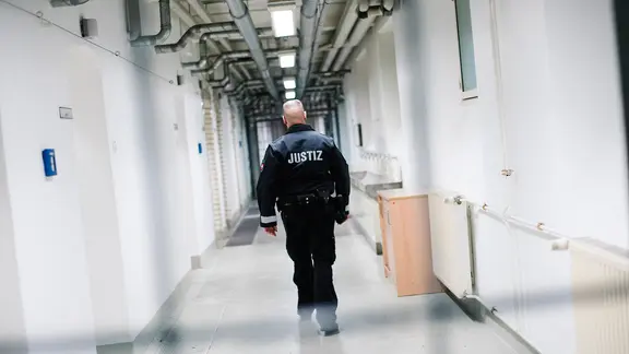 Ein Beamter des Justiz Vollzuges geht durch einen Gang in einem Gefängnistrakt.