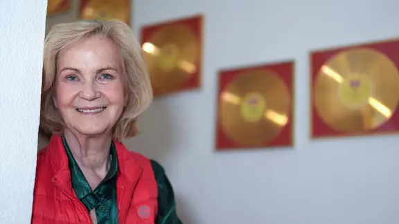 Eine ältere Frau lächelt, im Hintergrund hängen goldene Schallplatten an der Wand. | picture alliance/dpa | Marcus Brandt Eine ältere Frau lächelt, im Hintergrund hängen goldene Schallplatten an der Wand.
