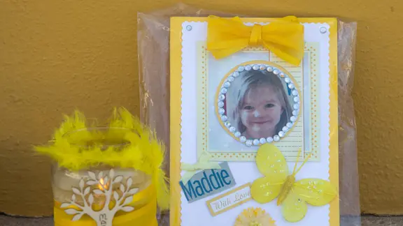 Eine Kerze und ein Foto von Madeleine McCann stehen zum Gedenken vor einer Wand.