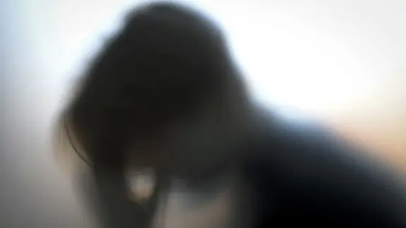 Ein junges Mädchen hält sich hinter einer Milchglasscheibe den Kopf. | picture alliance/dpa/Lehtikuva, Emmi Korhonen Ein junges Mädchen hält sich hinter einer Milchglasscheibe den Kopf.