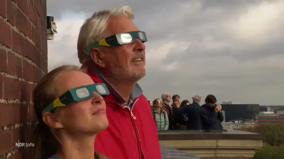 Ein Mann und eine Frau schauen mit Schutzbrillen nach oben in den Himmel.
