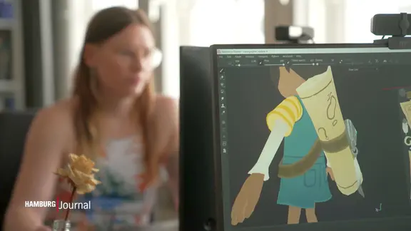 Spiele designen ist kleinteilig, da muss jeder Strich sitzen. | Screenshot NDR Eine junge Frau sitzt vor einem PC, auf einem Bildschirm ist eine kleine animierte Figur zu sehen.