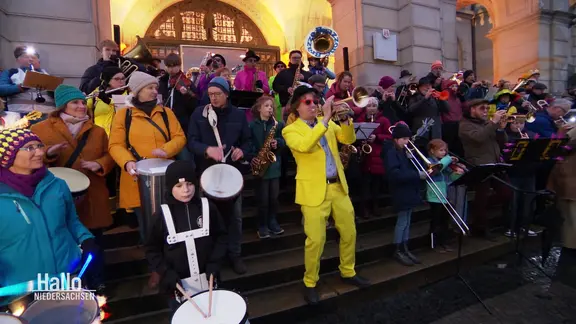 Auftritt der bunt gekleidetenBrass Band "Brazzo Brazzone" aus Erwachsenen und Kindern mit Blasinstrumenten und Trommeln. | Screenshot Auftritt der bunt gekleidetenBrass Band "Brazzo Brazzone" aus Erwachsenen und Kindern mit Blasinstrumenten und Trommeln.