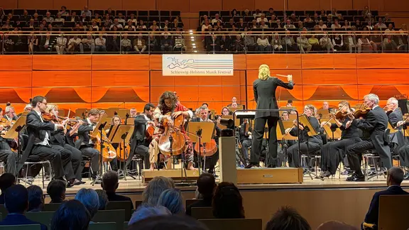 Das Eröffnungskonzert des SHMF in der Lübecker Musik- und Kongresshalle. | Linda Ebener / NDR Ein Orchester mit einer Cellistin und einer Dirigentin auf der Bühne.