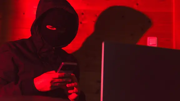 Ein maskierter Täter mit Handy und Laptop. (Themenbild) | CHROMORANGE, Michael Bihlmayer Ein maskierter Täter mit Handy und Laptop. (Themenbild)