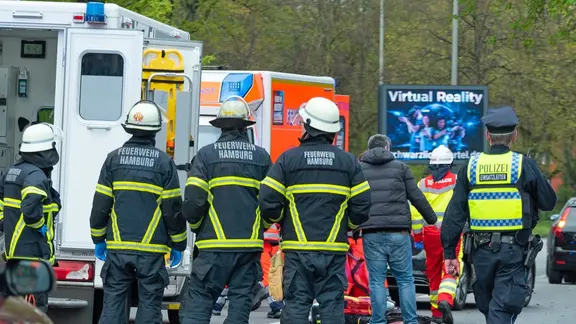 Feuerwehrleute und Einsatzfahrzeuge stehen nach einem Unfall in der Kieler Straße in Hamburg hinter einer zerstörten Ampel und zwischen Trümmerteilen. | dpa, Jonas Walzberg Feuerwehrleute und Einsatzfahrzeuge stehen nach einem Unfall in der Kieler Straße in Hamburg hinter einer zerstörten Ampel und zwischen Trümmerteilen.