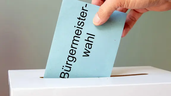 Eine Hand wirft den Stimmzettel für die Bürgermeisterwahl in die Urne. | Picture Alliance/ CHROMORANGE, Udo Herrmann Eine Hand wirft den Stimmzettel für die Bürgermeisterwahl in die Urne.