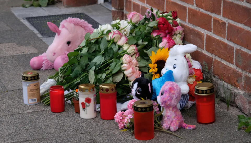 Blumen, Plüschtiere und Grablichter bilden eine Gedenkstelle vor einer Backsteinwand.