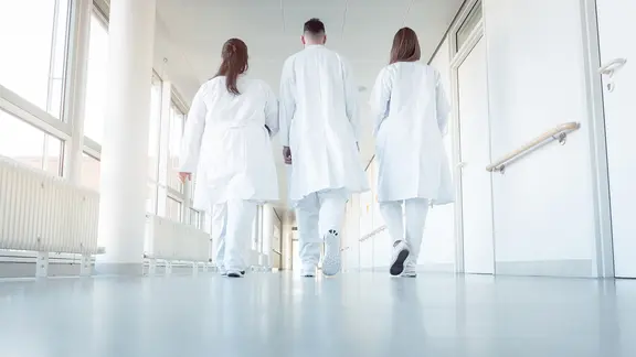 Zwei Ärztinnen und ein Arzt gehen auf einem Krankenhausflur entlang.