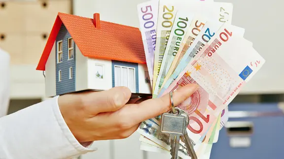 Ein Miniaturhaus und Geld liegen auf einer Hand.