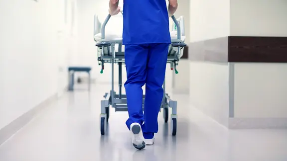 Eine Person schiebt ein Krankenhausbett über einen Flur