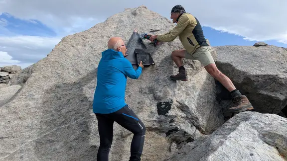 Zwei Personen entfernen eine Tafel an einem Berg | Alpenverein Salzburg Zwei Personen entfernen eine Tafel an einem Berg