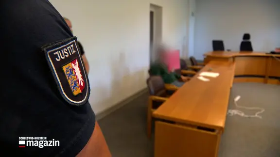 Ein Beamter der Justiz steht in einem Gerichtssaal bei einem Prozessauftakt. | NDR Ein Beamter der Justiz steht in einem Gerichtssaal bei einem Prozessauftakt.