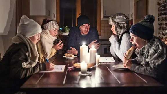 Fünf Personen sitzen in Winterkleidung an einem mit Kerzen beleuchteten Tisch. | Colourbox, Marian Vejcik Fünf Personen sitzen in Winterkleidung an einem mit Kerzen beleuchteten Tisch.