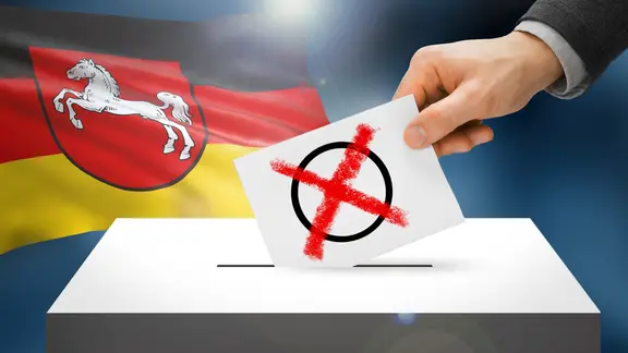 Wahlurne mit Wahlzettel, im Hintergrund das Landeswappen von Niedersachsen | Fotolia/niyazz/kebox, AdobeStock, joric Wahlurne mit Wahlzettel, im Hintergrund das Landeswappen von Niedersachsen