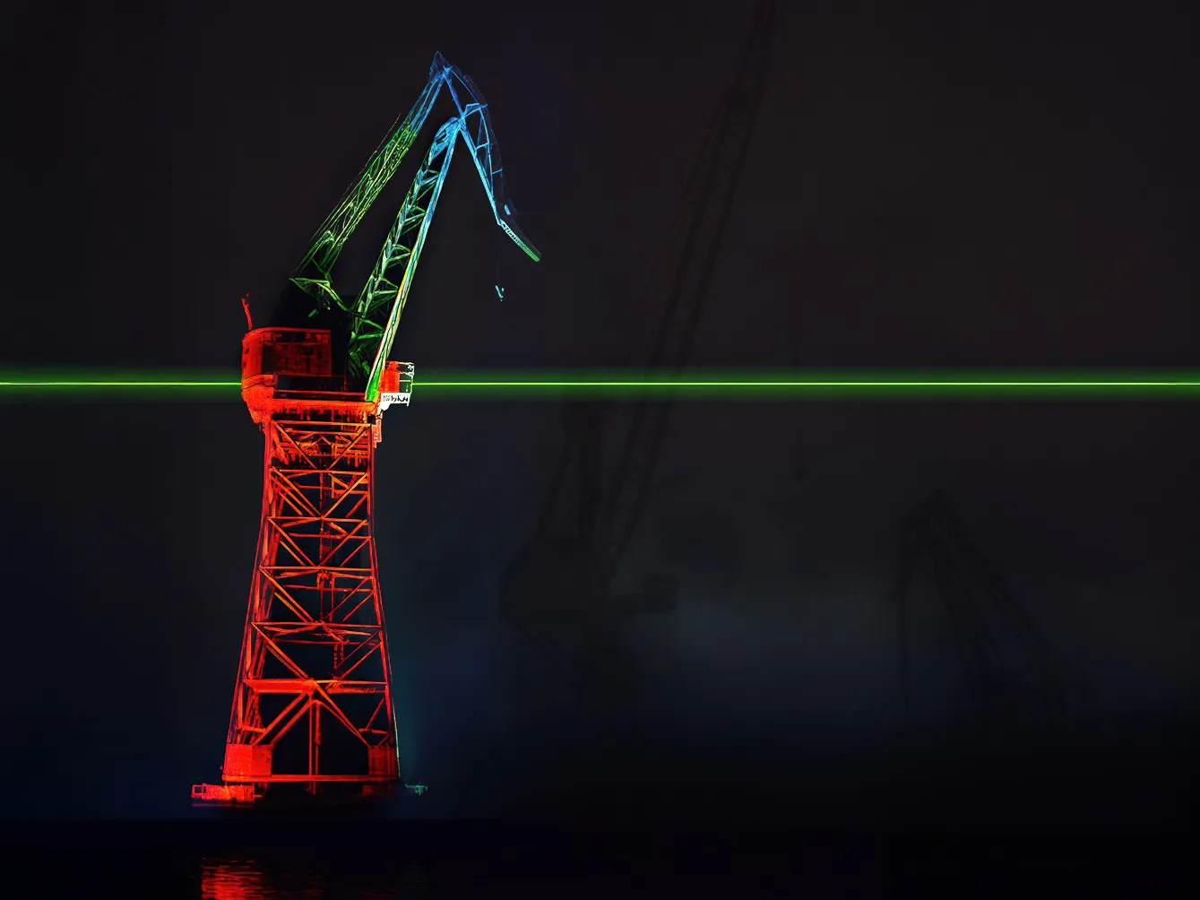Valolla punaiseksi värjätty nostokurki, jonka läpi menee vihreä laserviiva