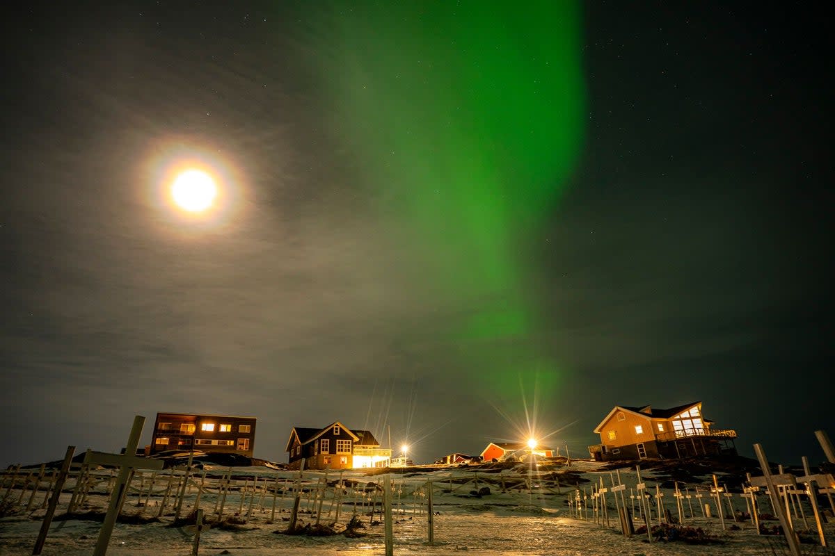 The Aurora Borealis, also known as the Northern Lights, shines over houses and a graveyard in Nuuk, Greenland (PA)