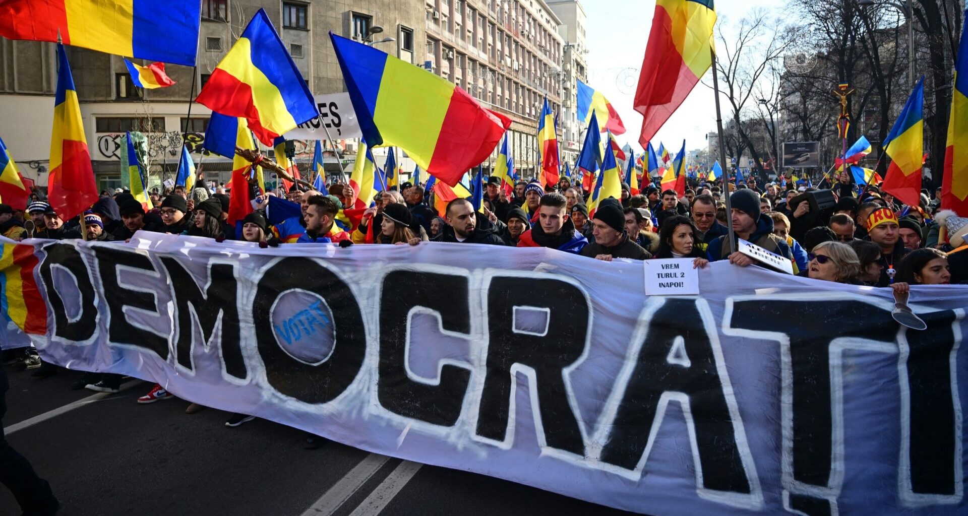 Supporters of right-wing nationalist party AUR and of presidential candidate Călin Georgescu hold a banner reading “democracy” as they march in Bucharest on January 12, 2025 to protest against the annulment of the second tour of the presidential election asking president Iohannis resign.