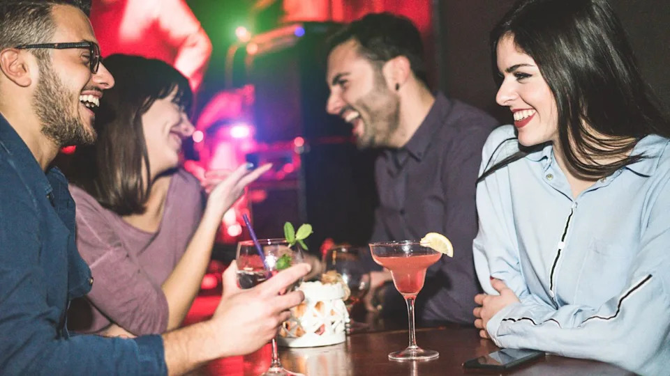 Happy friends having fun at club jazz bar - Young trendy people drinking tropical cocktails and laughing together - Party and nightlife concept - Focus on right woman face - Warm filter